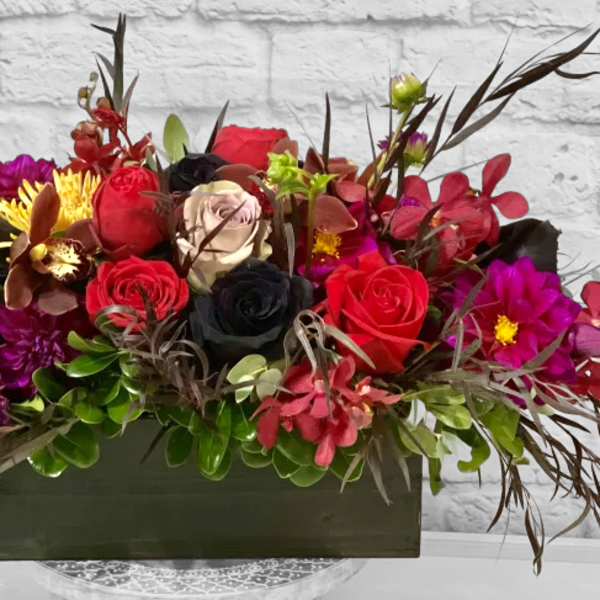 Rectangular floral arrangement with red, black, and purple blooms in a dark container