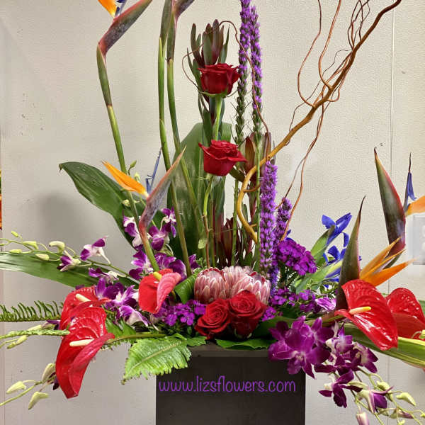 Tall tropical floral arrangement with red roses and purple orchids in a black container