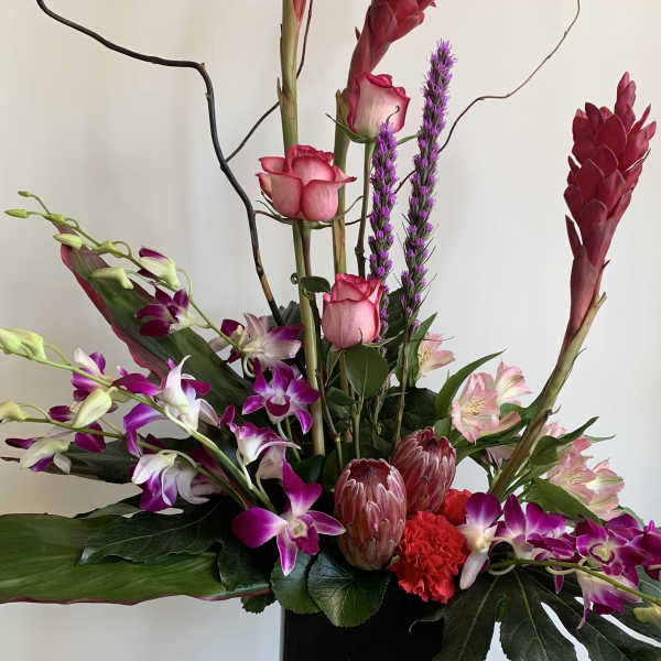 Tall floral arrangement with pink roses, purple orchids, and red tropical blooms in a black vase