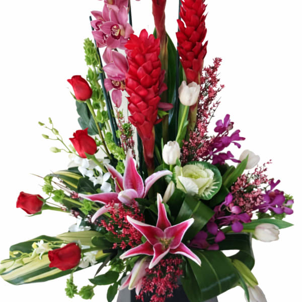 Tall floral arrangement with red and pink orchids, lilies, and roses in a black vase