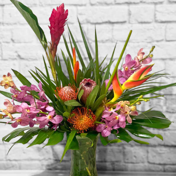 Tropical bouquet with orchids and orange blooms in a glass vase