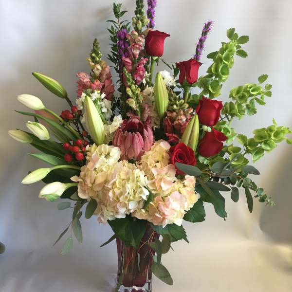 Tall mixed bouquet with red roses, lilies, hydrangeas, and greenery in a glass vase