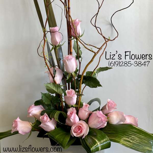Tall arrangement of pink roses with curly branches and broad leaves