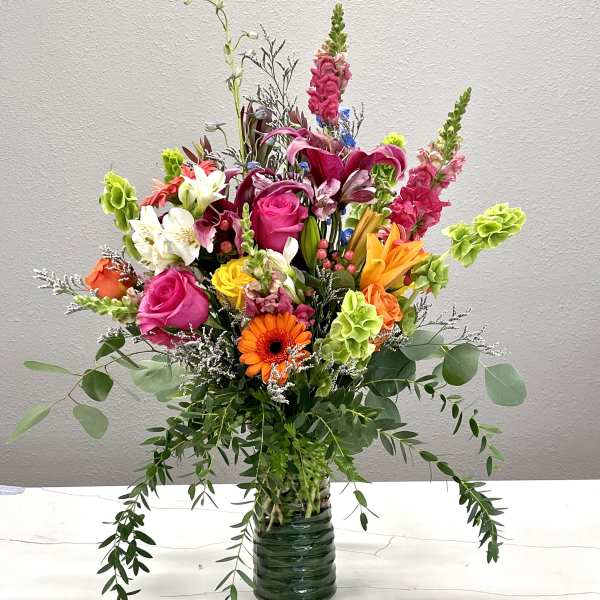 Colorful mixed bouquet in a glass vase with roses, lilies, and gerbera daisies