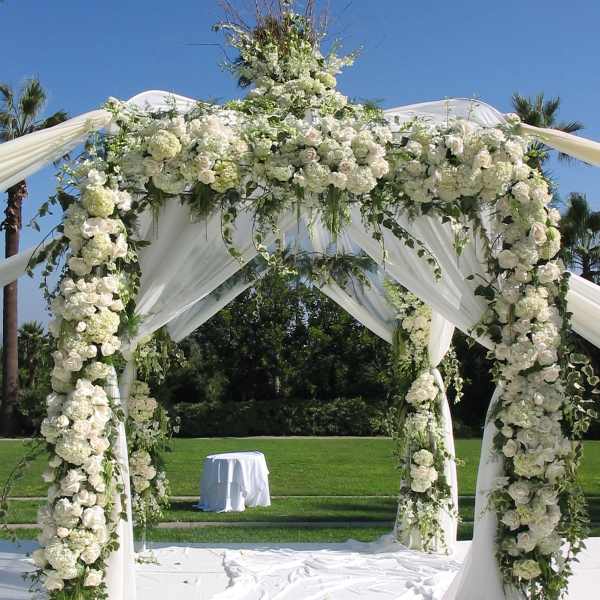 White floral wedding arch draped with fabric outdoors