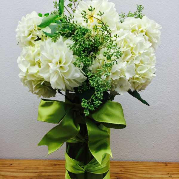 White flower bouquet in a glass vase with a green ribbon