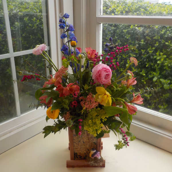 Colorful mixed flower arrangement in a wooden container on a windowsill