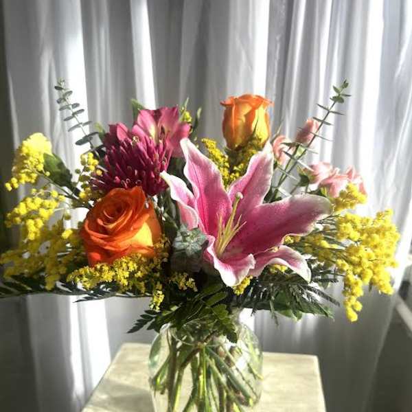 Mixed bouquet with pink lilies, orange roses, and yellow filler in a glass vase