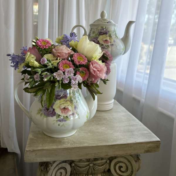 Pastel flower arrangement in a floral teapot vase on a table