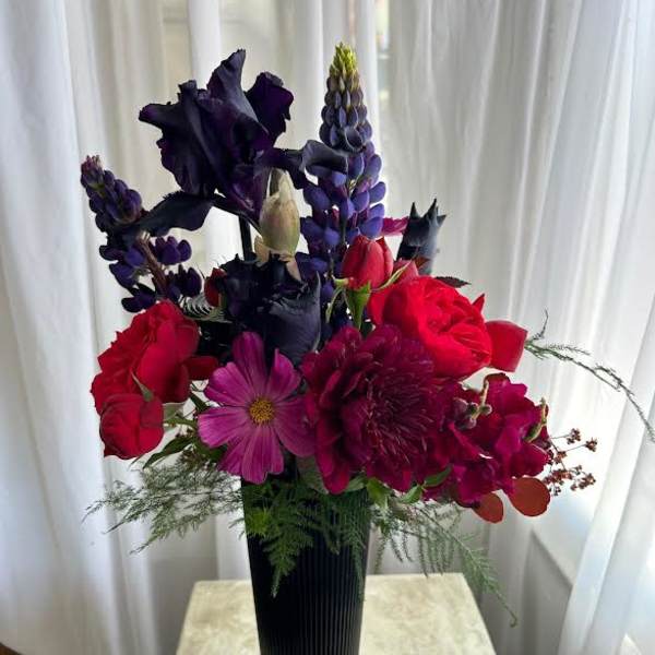 Tall bouquet of red and purple flowers in a black vase