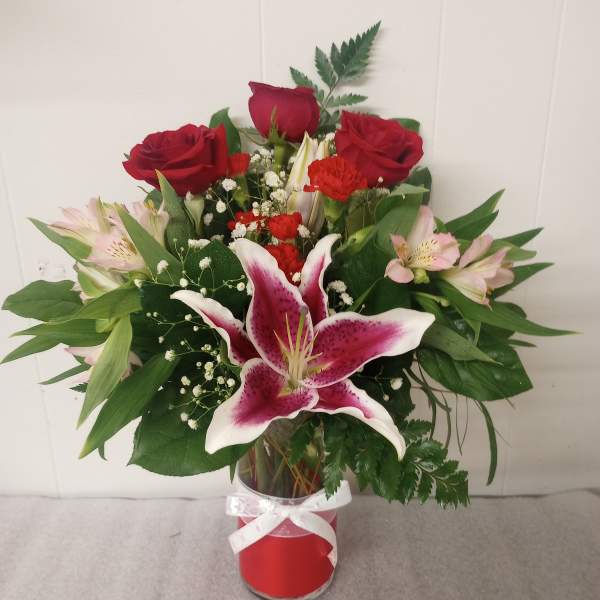 Red roses and pink lilies in a glass vase with a white ribbon