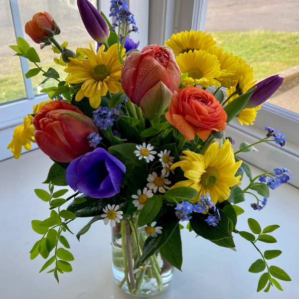 Colorful mixed bouquet in a clear glass vase with tulips, daisies, and ranunculus