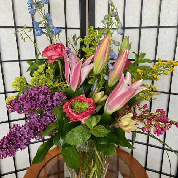 Mixed bouquet with pink lilies, purple hydrangea, and blue delphinium in a glass vase