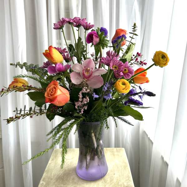 Mixed bouquet in a purple glass vase with roses, orchids, and daisies