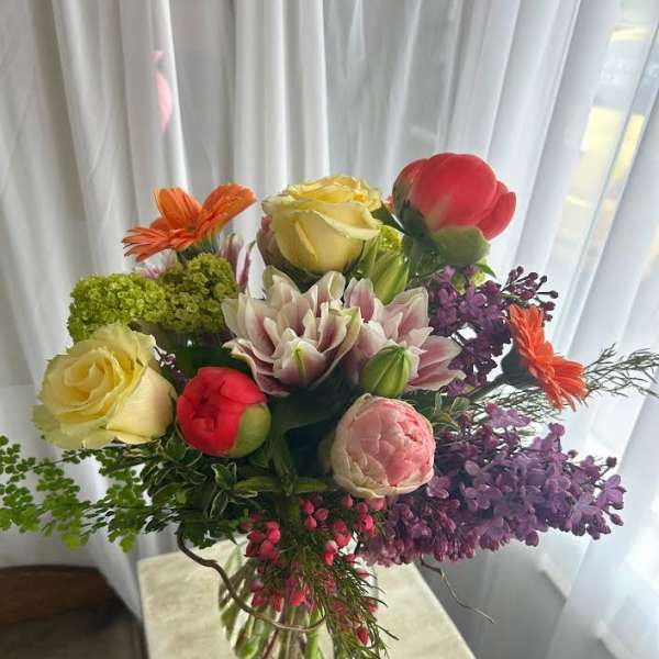 Mixed bouquet of roses, lilies, and purple blooms in a clear glass vase