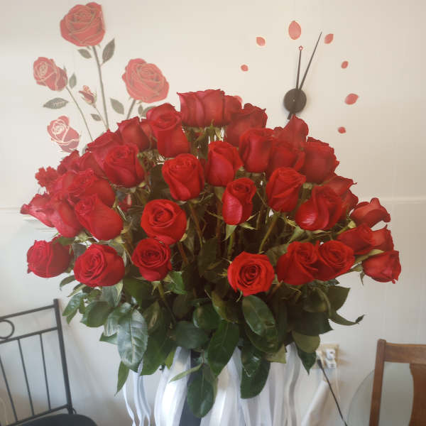 Large bouquet of red roses in a black vase with white ribbon streamers