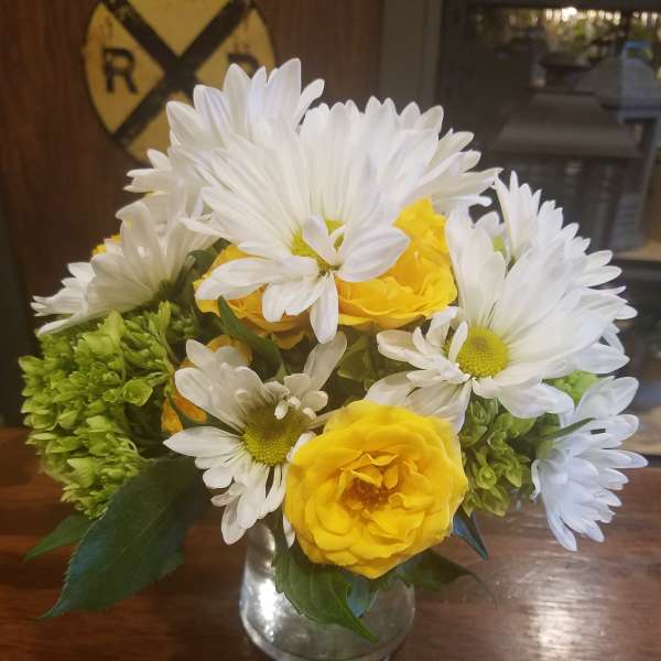 Yellow roses and white daisies arranged in a clear glass vase