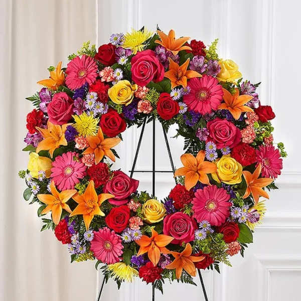 Colorful floral wreath on a black stand with roses, lilies, and daisies