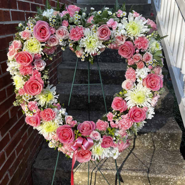 Heart-shaped floral wreath with pink roses and white daisies on a stand