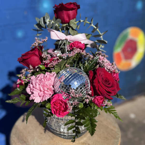 Pink and red roses arranged around a mirrored disco ball in a glass vase