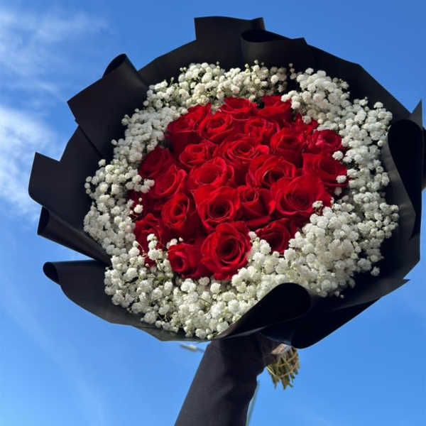 Bouquet of red roses surrounded by white baby's breath in black wrap