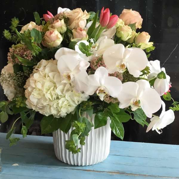 White orchids and pale roses arranged in a ribbed white vase