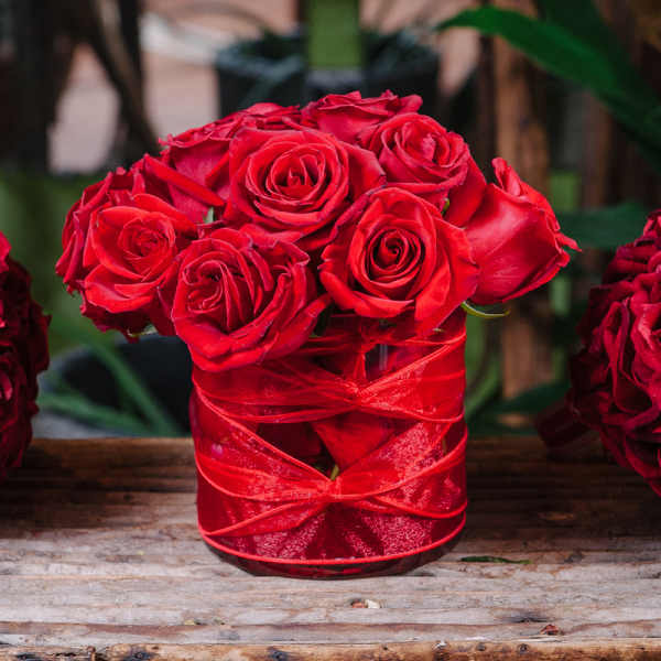 Red roses arranged in a glass vase wrapped with red ribbon