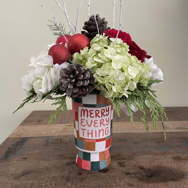 Holiday floral arrangement in a patterned vase with red ornaments and pinecones