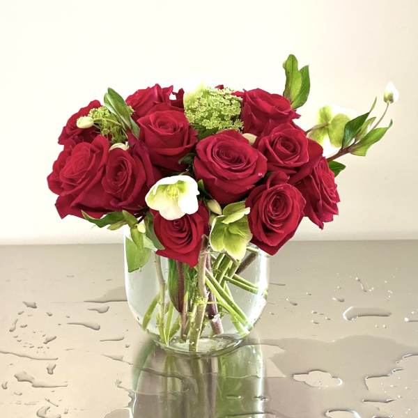 Red roses arranged in a clear glass vase with white flowers