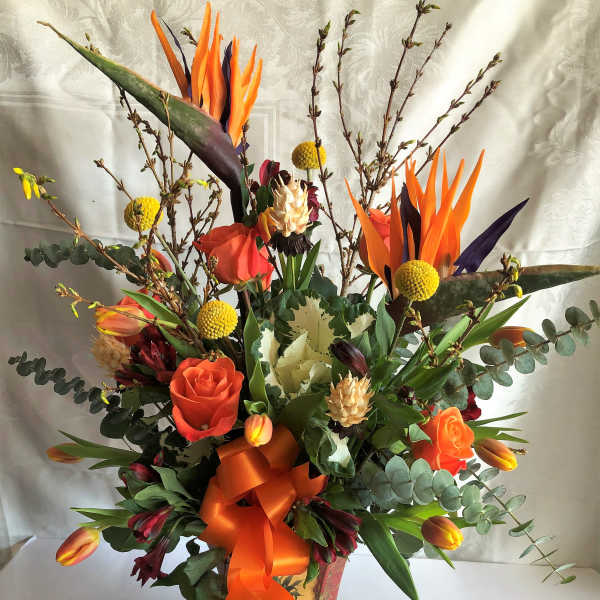 Orange and red floral arrangement in a decorative vase with ribbon
