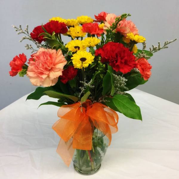 Bouquet of red, yellow, and peach carnations in a glass vase with an orange ribbon
