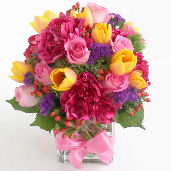 Pink and yellow mixed flower bouquet in a clear glass vase with a pink ribbon