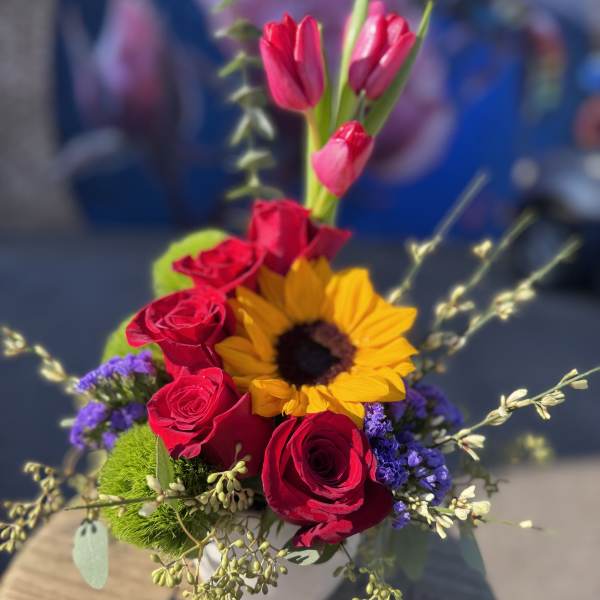 Bouquet of red roses, pink tulips, and a sunflower in a white vase