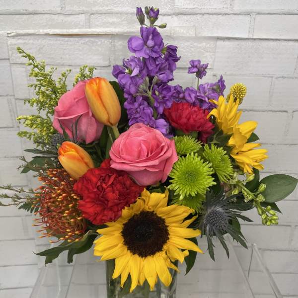 Mixed bouquet with roses, tulips, sunflowers, and purple blooms in a glass vase