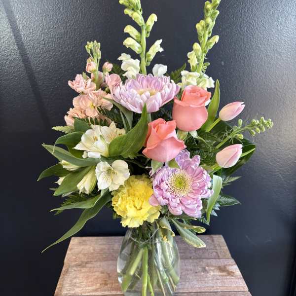 Mixed bouquet in a glass vase with pink roses, lilies, and pastel blooms