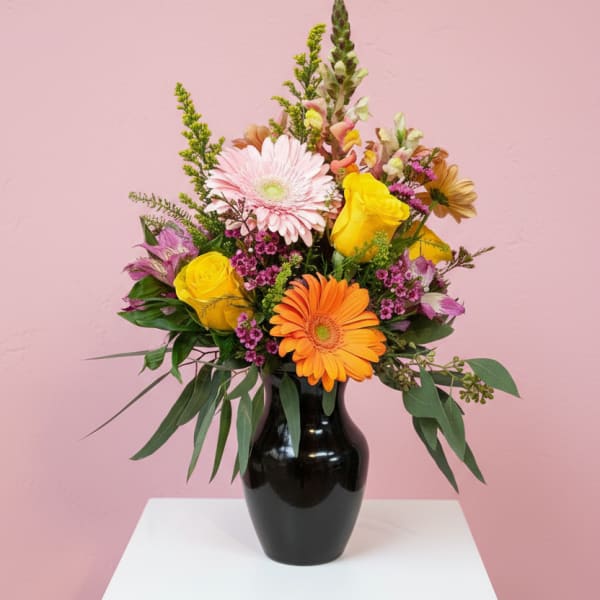 Mixed bouquet in a black vase with pink, yellow, and orange blooms