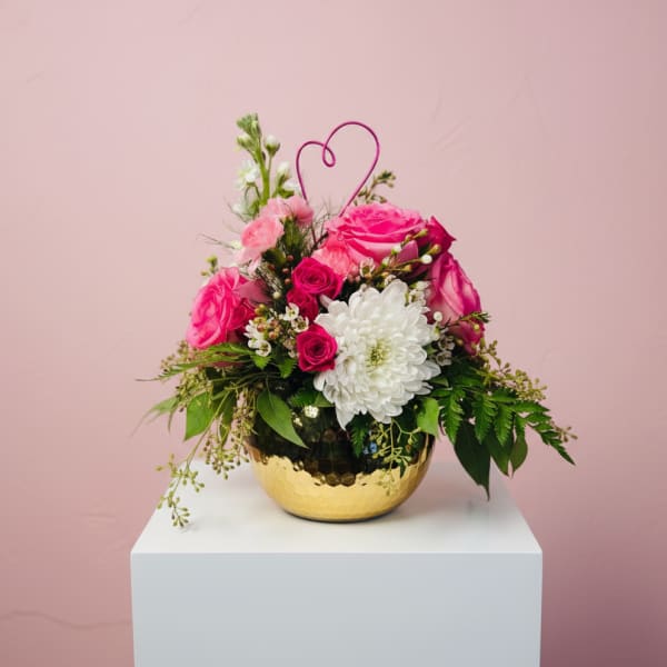Pink and white flower arrangement in a gold bowl with a heart pick