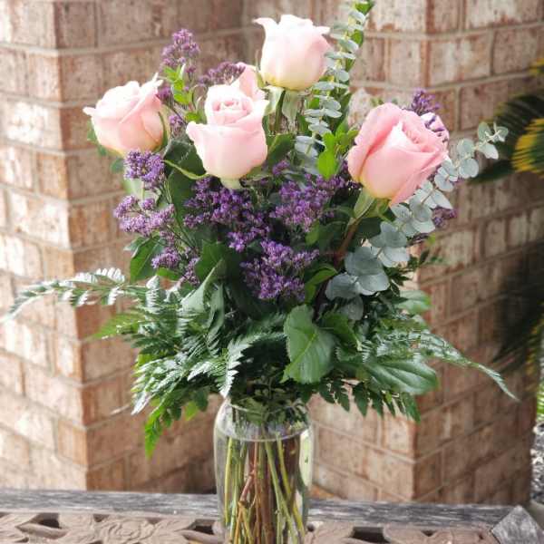 Pink roses and purple filler flowers in a clear glass vase