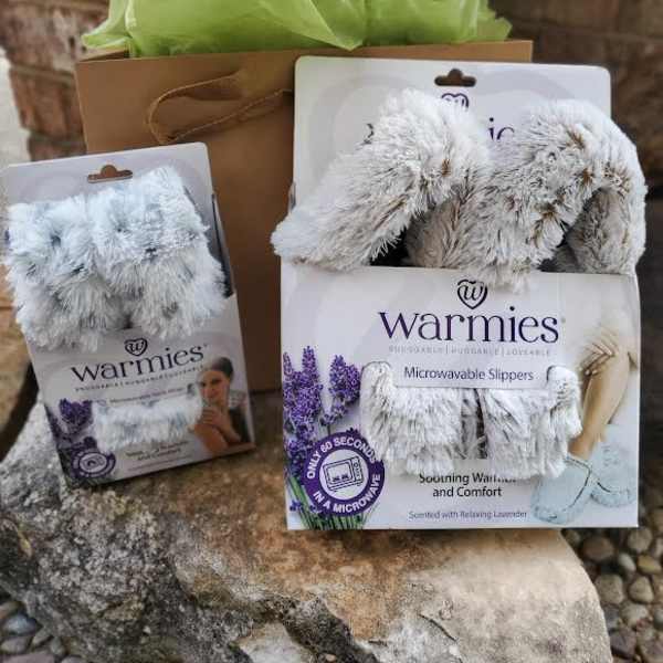Gift set with two pairs of fuzzy slippers in packaging and a brown bag with green tissue paper