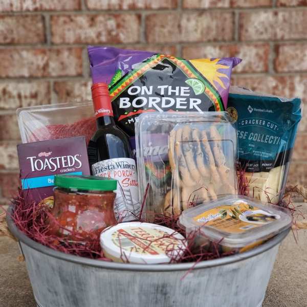 Gift basket with wine, crackers, chips, dip, and snacks in a metal tub