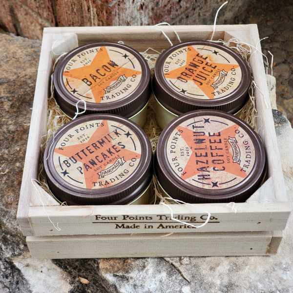 Four scented candles in a wooden crate with straw filler