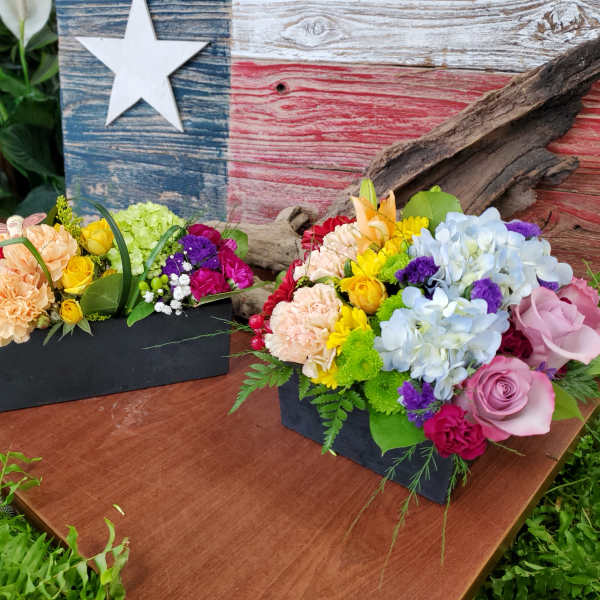 Two colorful floral arrangements in black boxes on a wooden table