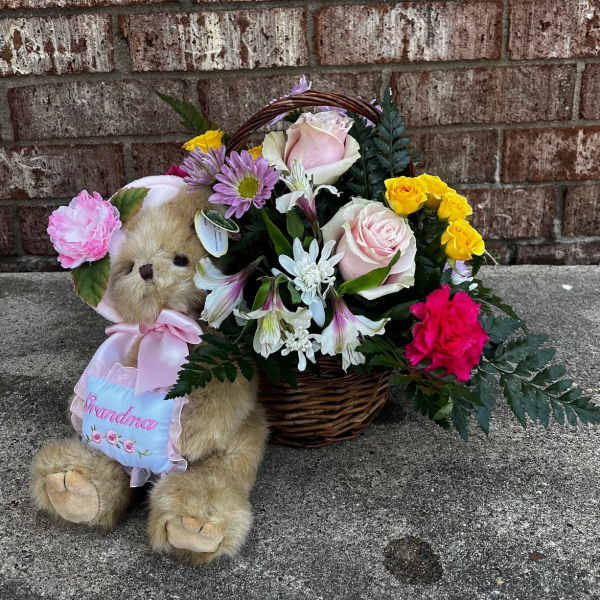 Teddy bear beside a basket of pink, yellow, and white flowers