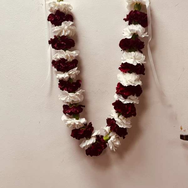 Two white and burgundy flower garlands hang on a wall.