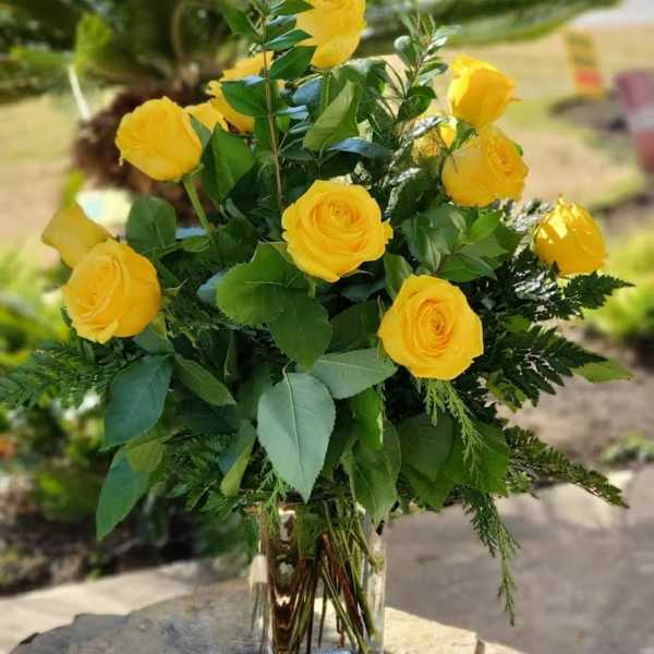 Tall arrangement of yellow roses with lush greenery in a clear glass vase