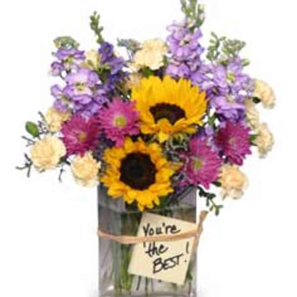 Bouquet of sunflowers, purple flowers, and cream blooms in a glass vase