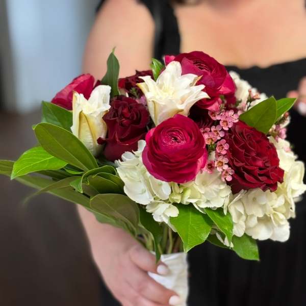 Handheld bouquet of red and white flowers with green leaves