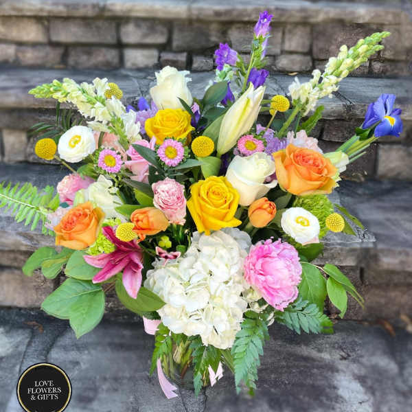 Colorful mixed bouquet of roses, lilies, hydrangea, peony and other blooms in a clear glass vase