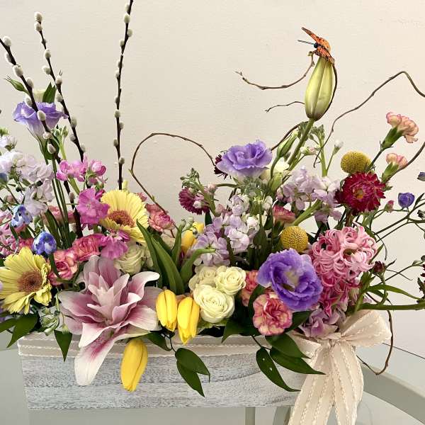 Mixed floral arrangement in a rectangular container with pink, purple, yellow, and white blooms