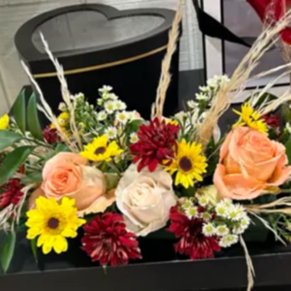 Low floral arrangement with peach and white roses and yellow daisies in a black container